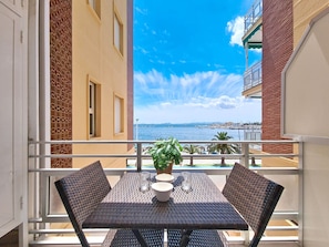 Ein Balkon mit Tisch und Stühlen, einer Topfpflanze und Blick auf das Meer und Gebäude.