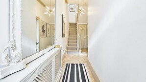 A hallway with a herringbone floor, a black and white striped rug, a white radiator, and a staircase with a beige carpet. - 2 Bed Luxury Chelsea Townhouse Sleeps 5 (London)