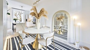 A dining area with a round table, chairs, a vase with pampas grass, a mirror, and a floor lamp. - 2 Bed Luxury Chelsea Townhouse Sleeps 5 (London)