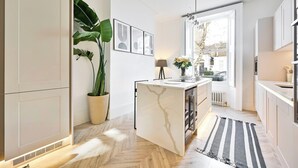 A modern kitchen with a marble island, potted plants, and a view through the window. - 2 Bed Luxury Chelsea Townhouse Sleeps 5 (London)
