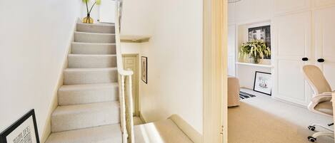 A staircase leading to a room with a white door, a framed picture, and a vase with flowers.