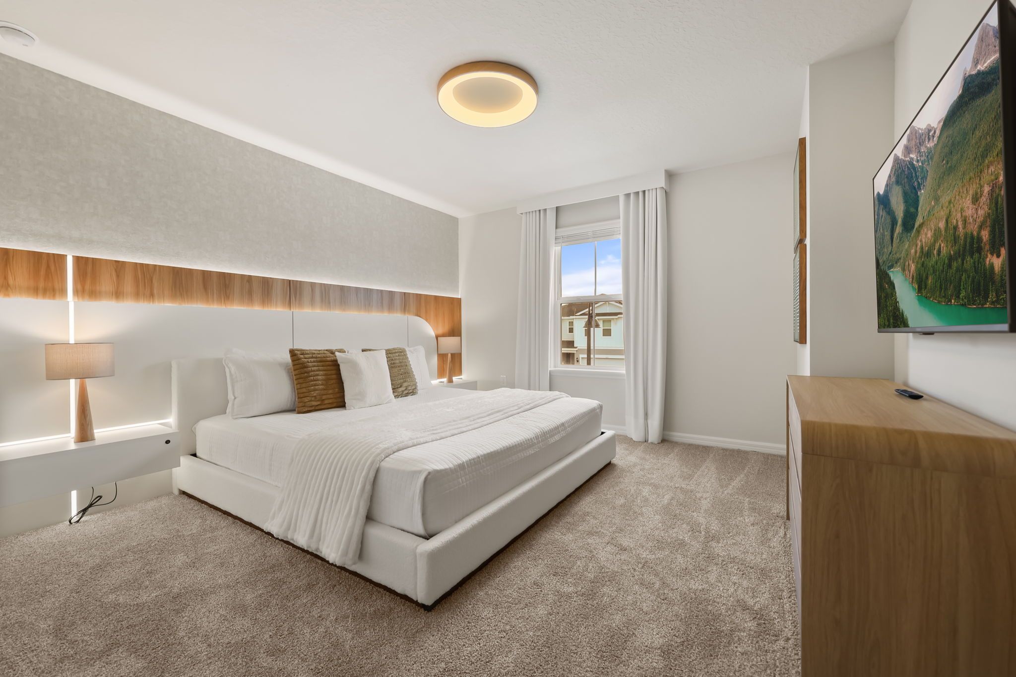 A modern bedroom with a large bed, a nightstand, a desk, and a TV on the wall.