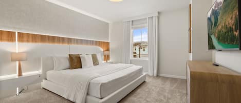 A modern bedroom with a large bed, a nightstand, a desk, and a TV on the wall.