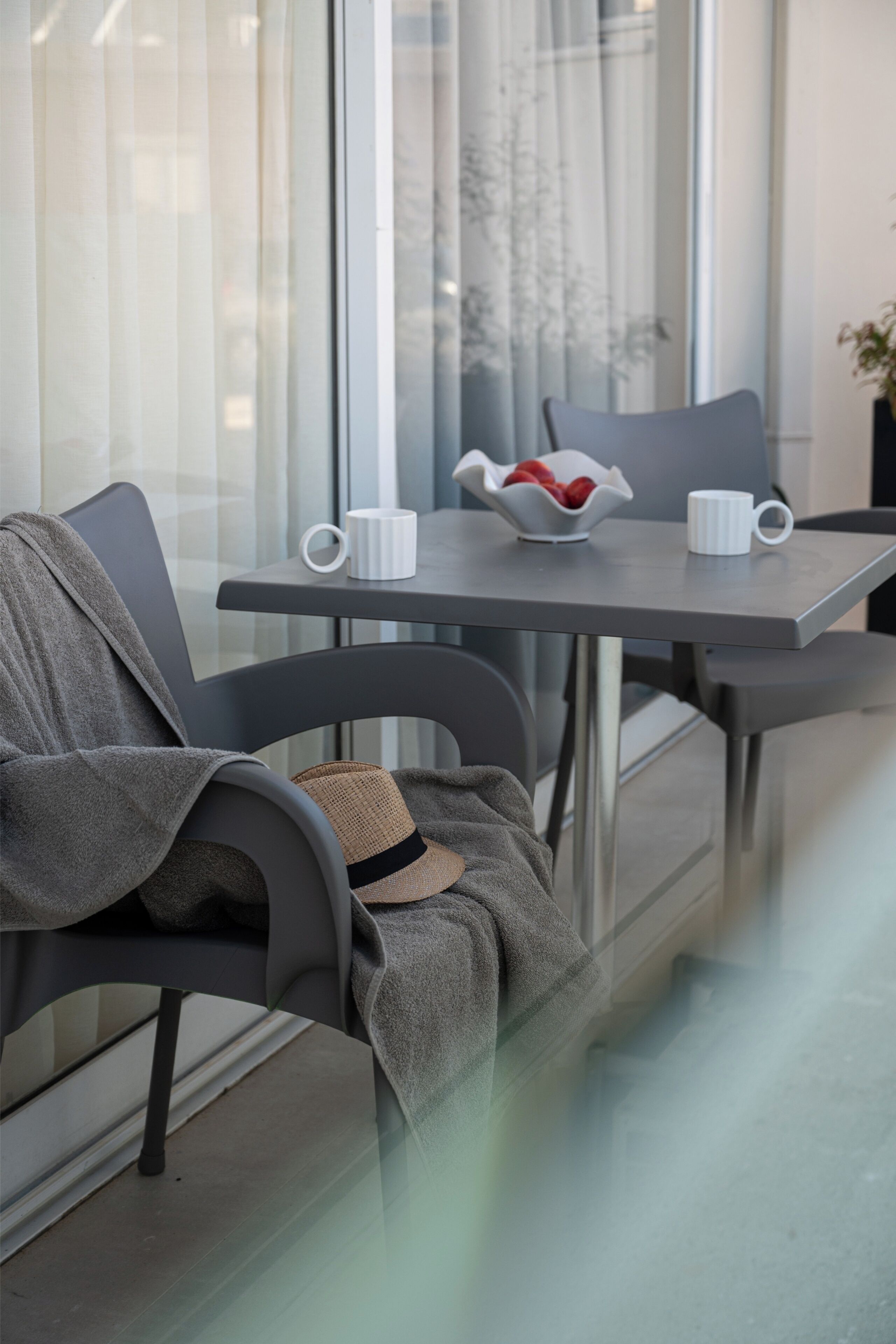 A modern room with a glass table, two chairs, a bowl of fruit, and a white mug.