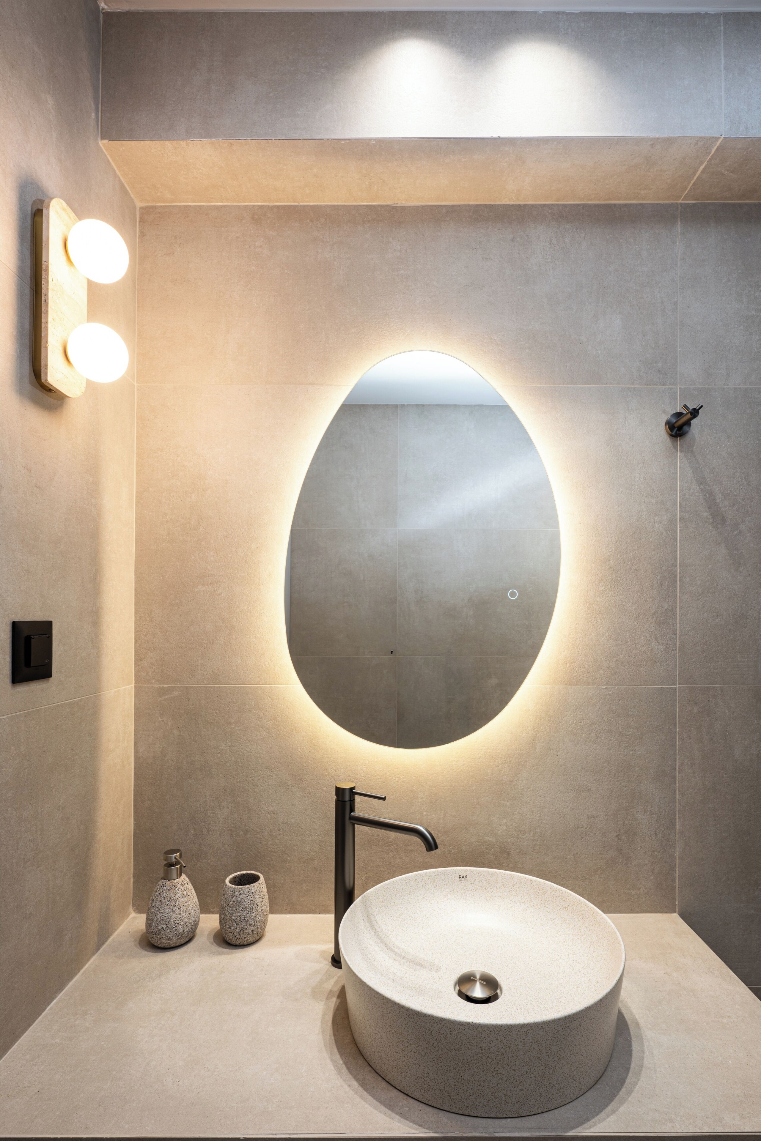 A modern bathroom with a round mirror, a vessel sink, and two wall-mounted lights.