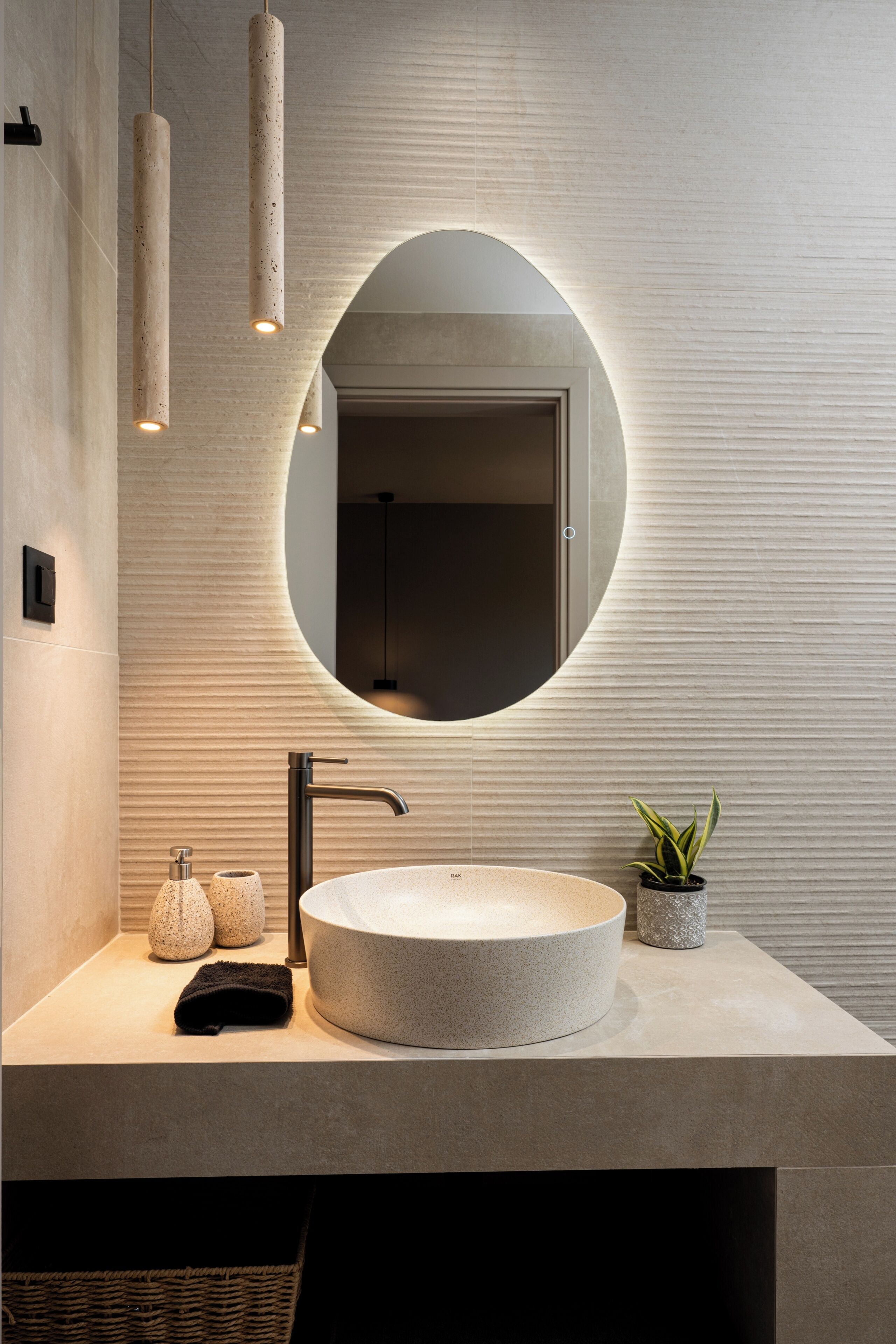 Un baño moderno con un espejo redondo, un lavabo circular, una toalla, una planta en maceta y lámparas colgantes.