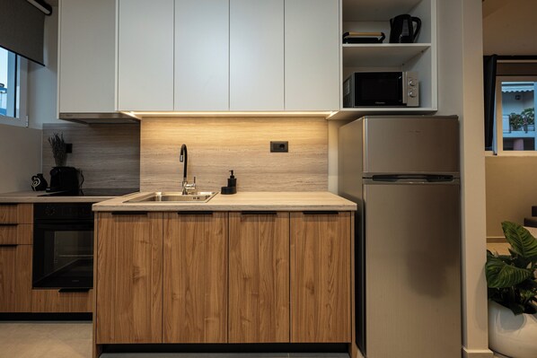 A modern kitchen with wooden cabinets, a stainless steel refrigerator, a microwave, and a built-in oven. - Elmar Urban Living (Chania)