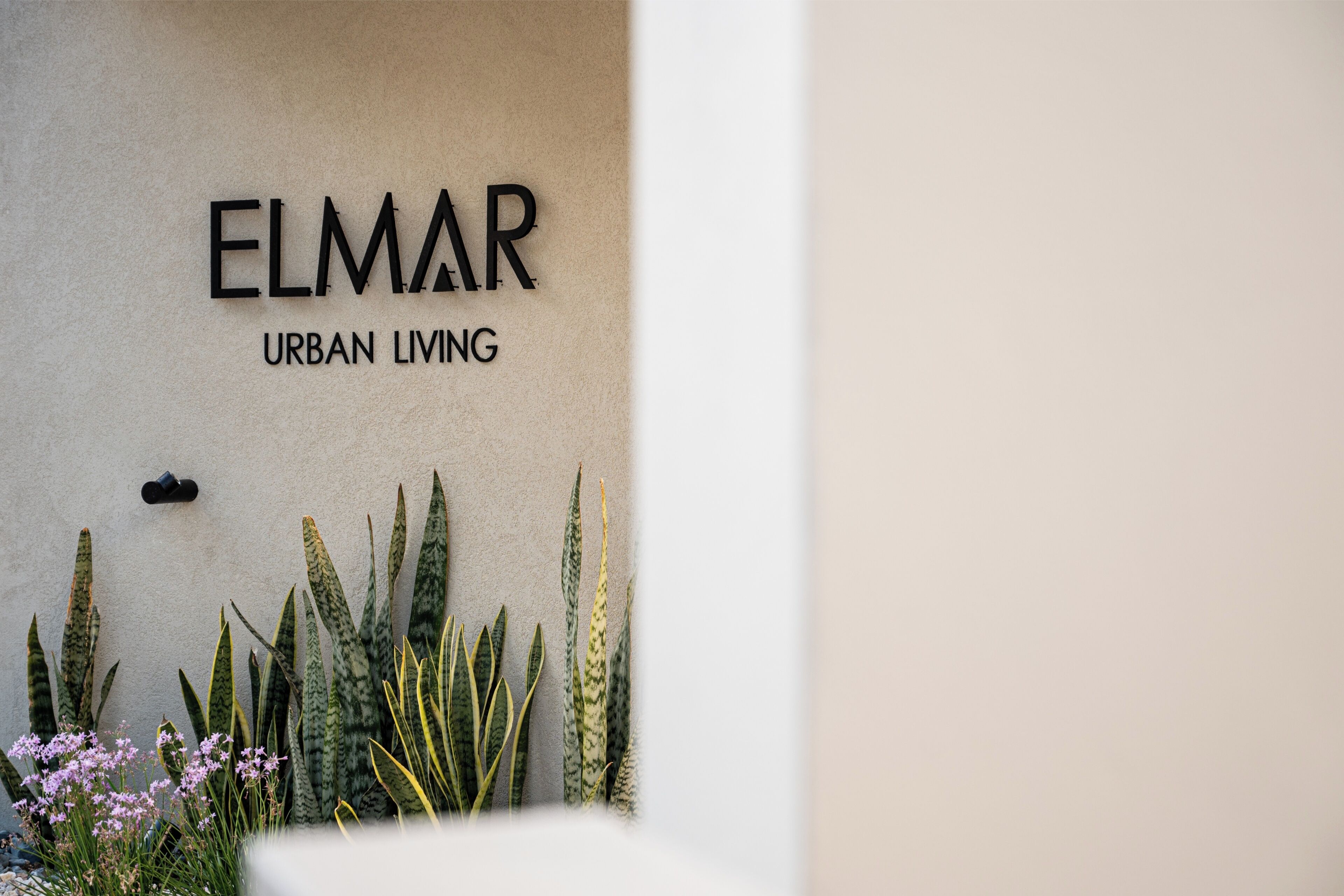 Een muur met de tekst 'ELMAR URBAN LIVING' en een klein zwart object erboven.