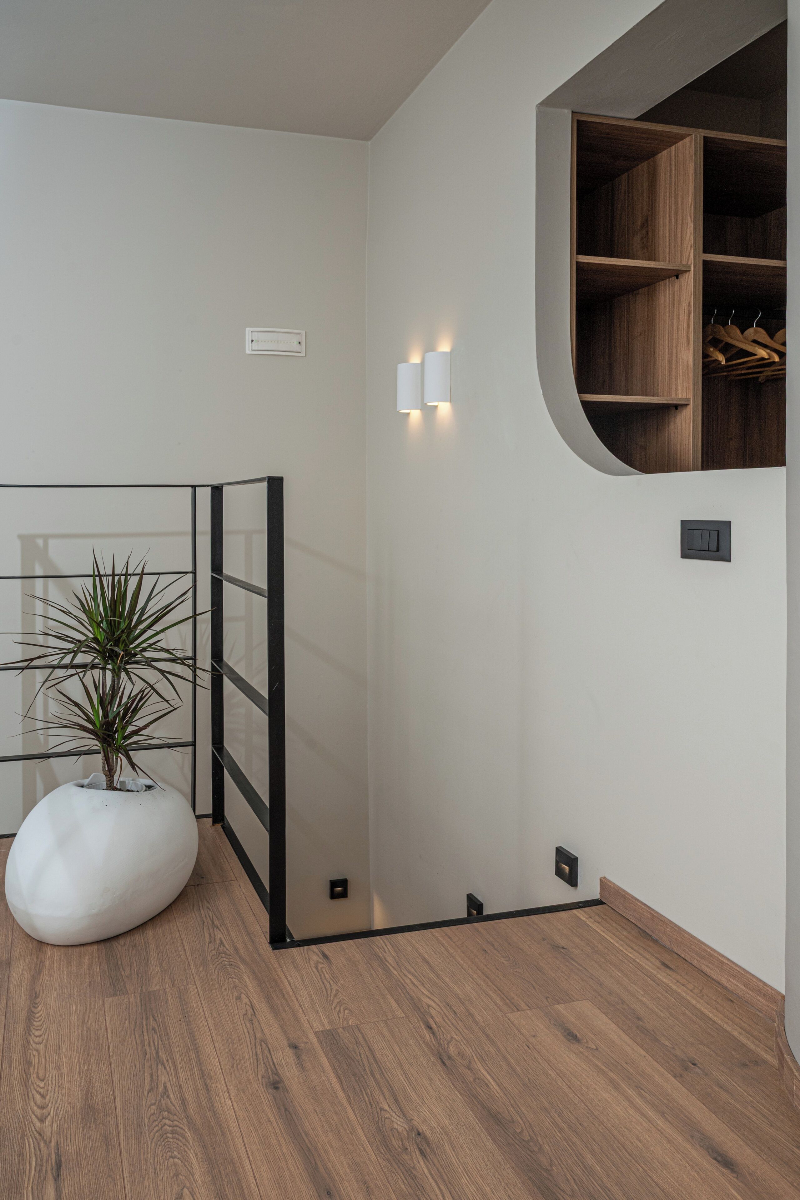 Ein modernes Zimmer mit Holzboden, einer weißen Topfpflanze, einer schwarzen Trennwand und einer Holzregaleinheit mit hängenden Gegenständen.