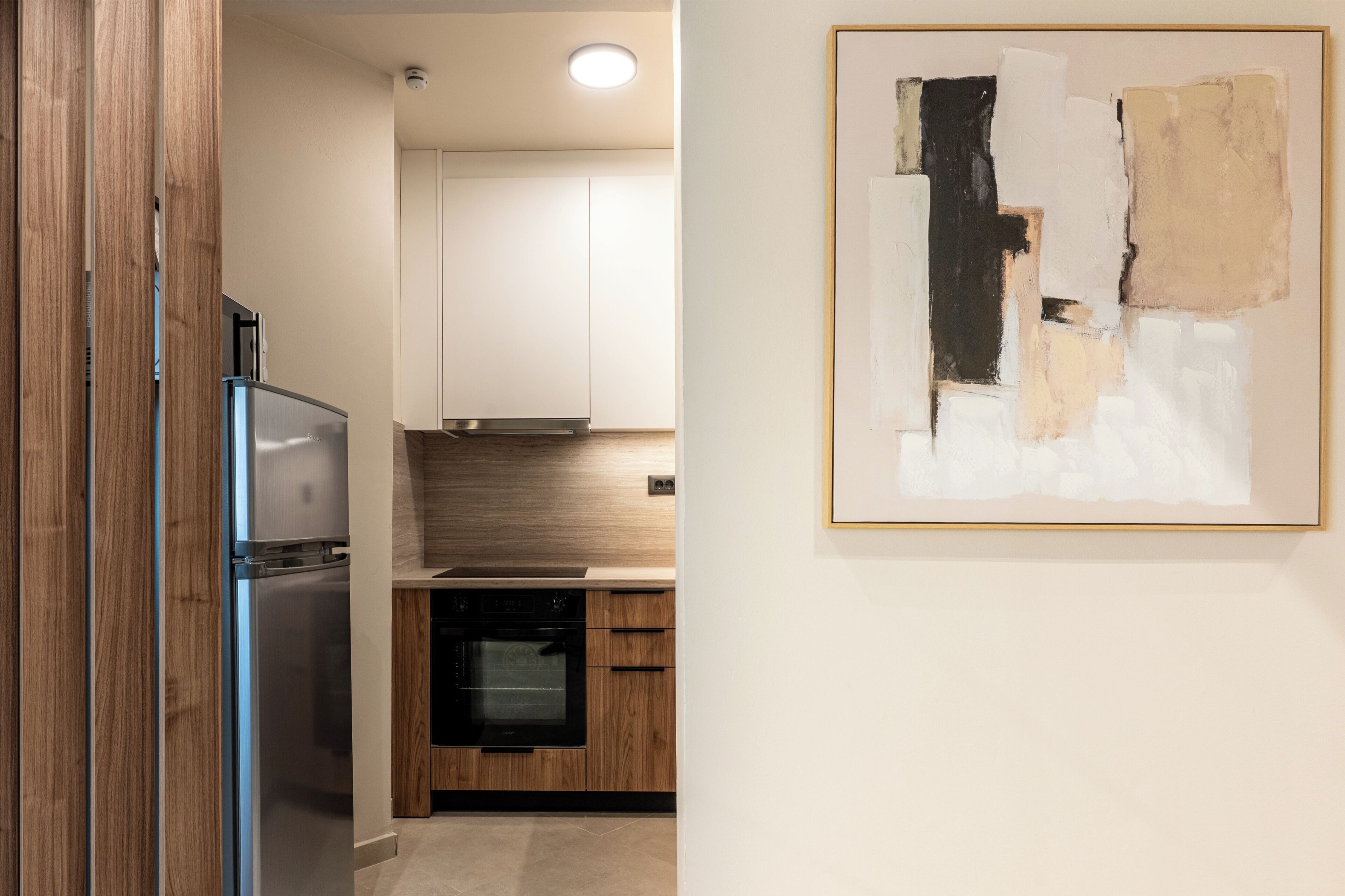 A modern kitchen with stainless steel appliances, wooden cabinets, and a minimalist artwork on the wall.