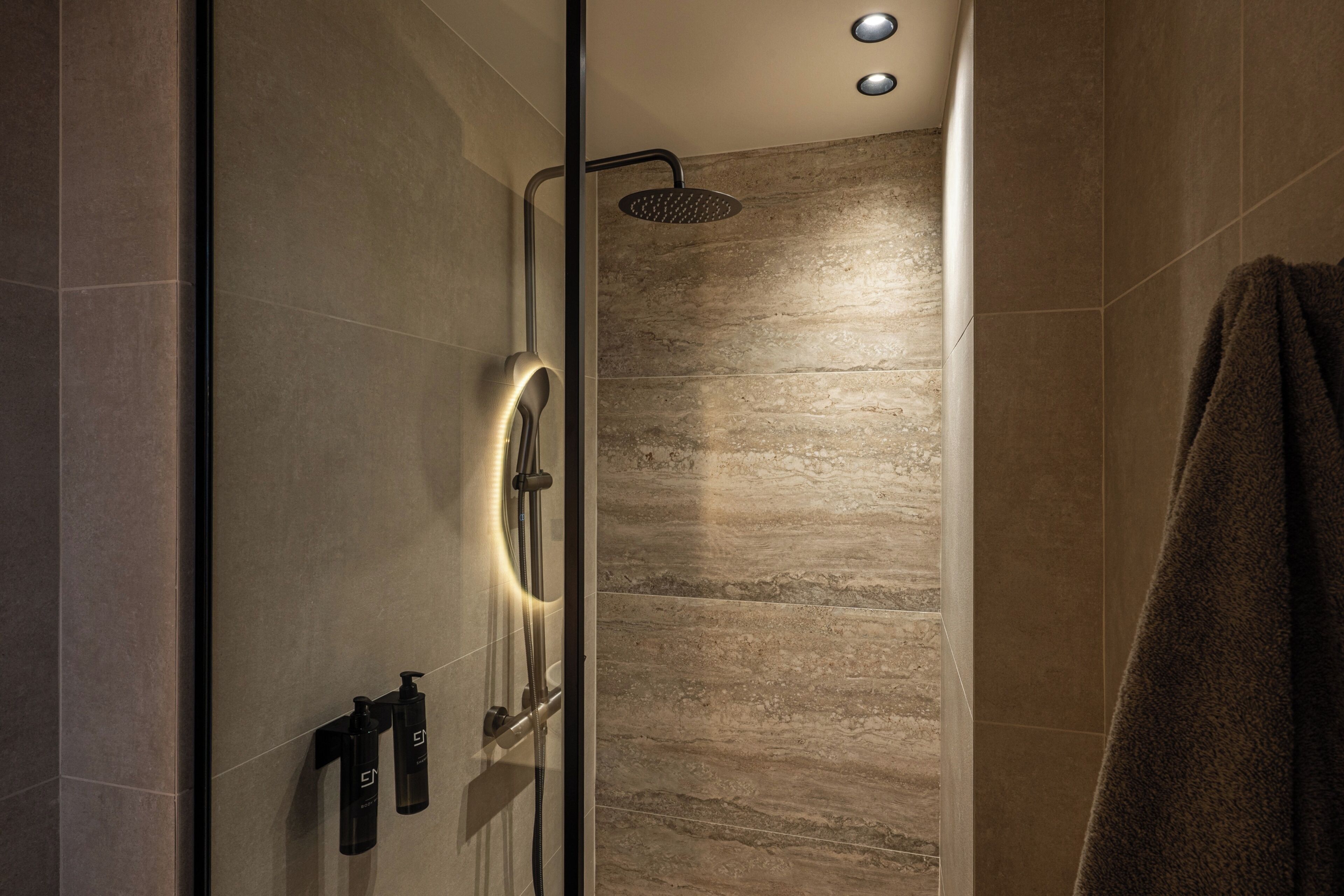 Ein modernes Badezimmer mit Duschkabine aus Glas, Handtuchhalter und Wandseifenspender.