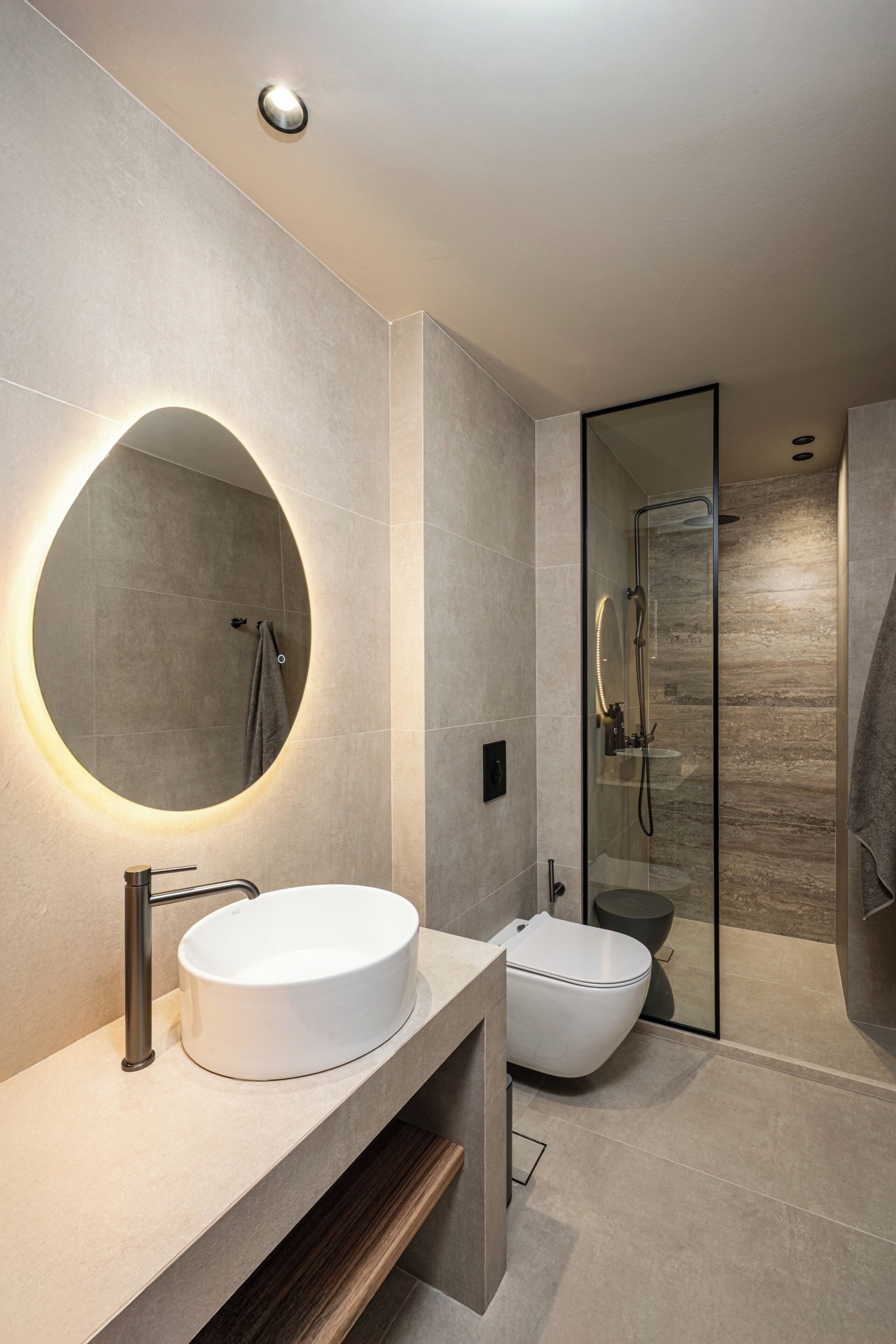A modern bathroom with a round mirror, a sink, a toilet, and a glass-enclosed shower.