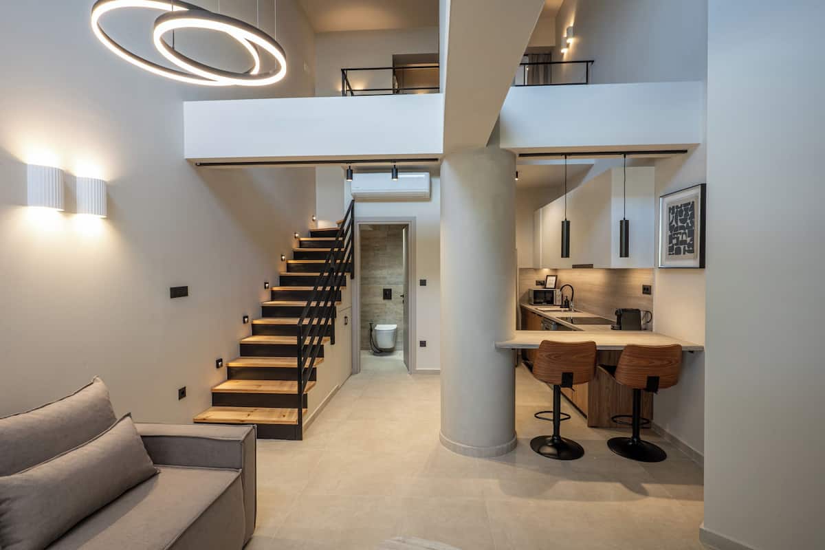 Ein modernes Interieur mit einer Treppe, einer Küchenzeile mit Barhocker und einer Sitzecke mit einer Couch.
