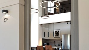 A modern kitchen with a stainless steel refrigerator, a dining area with two chairs, and a mezzanine level with a staircase. - Elmar Urban Living (Chania)