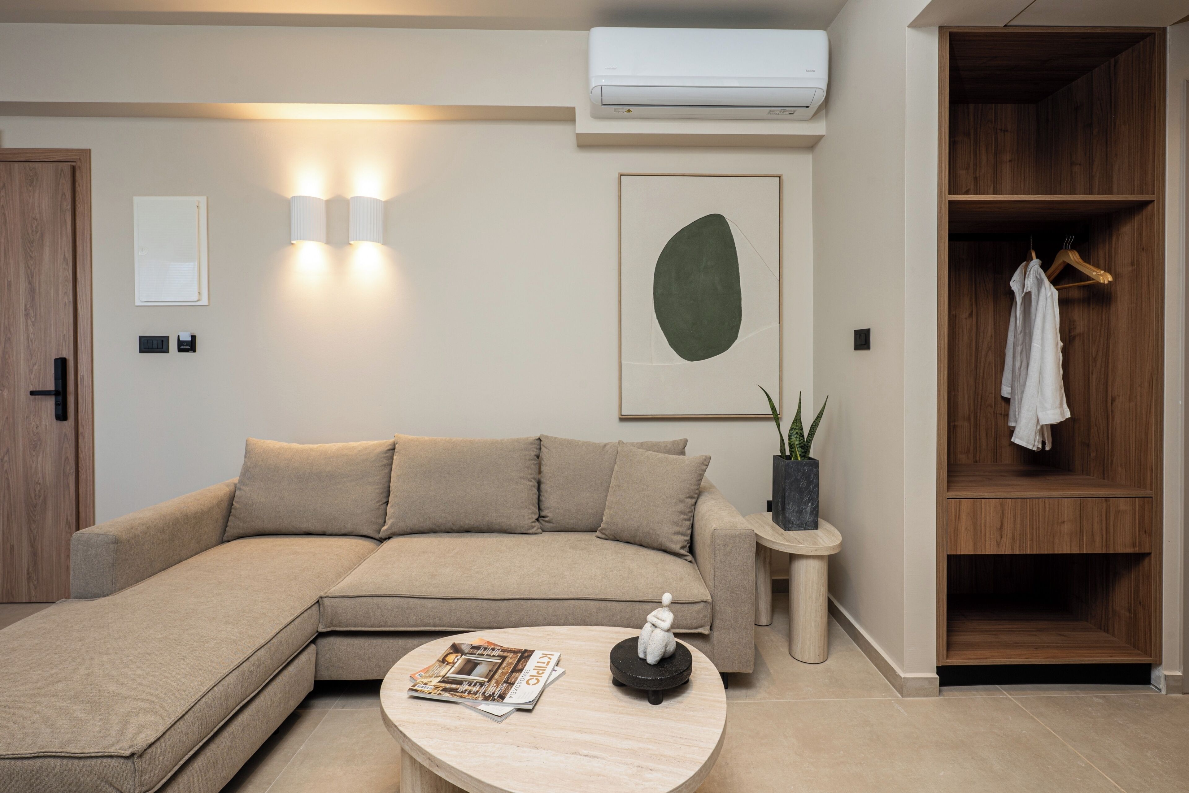 A modern living room with a sectional sofa, a round coffee table, a wall-mounted air conditioner, and a wooden wardrobe.