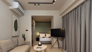 A modern hotel room with a sofa, a round coffee table, a flat-screen TV, and a large window with curtains. - Elmar Urban Living (Chania)