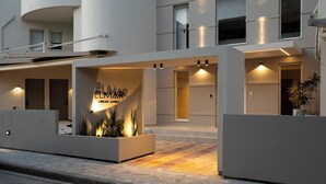 A modern building with a prominent entrance, illuminated signage, and a landscaped area with plants. - Elmar Urban Living (Chania)