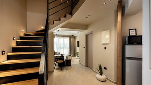 A modern interior with a wooden staircase, a dining area with a table and chairs, a refrigerator, and a potted plant. - Elmar Urban Living (Chania)