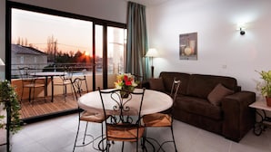 A living room with a sofa, a dining table with chairs, a balcony with a view of the sunset, and a potted plant. - Provencal Studio for 4 in Sorgue (L'Isle-sur-la-Sorgue)