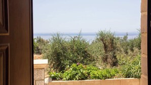 An open door leading to a view of a garden with various plants and a distant body of water. - Emilia's Guest House with Sea View Balcony, Stoupa (Stoupa)