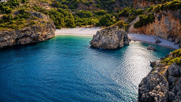 A coastal landscape with a rocky outcrop, clear turquoise water, and a white sandy beach. - Emilia's Guest House with Sea View Balcony, Stoupa (Stoupa)