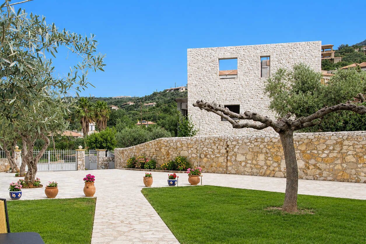 A stone building with a paved pathway, potted plants, and a tree.
