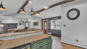 A kitchen with a large island, wooden ceiling beams, pendant lighting, and a clock on the wall. - Rustic Woodland Cabin | Hot Tub | Cozy Escape (Lake Harmony)
