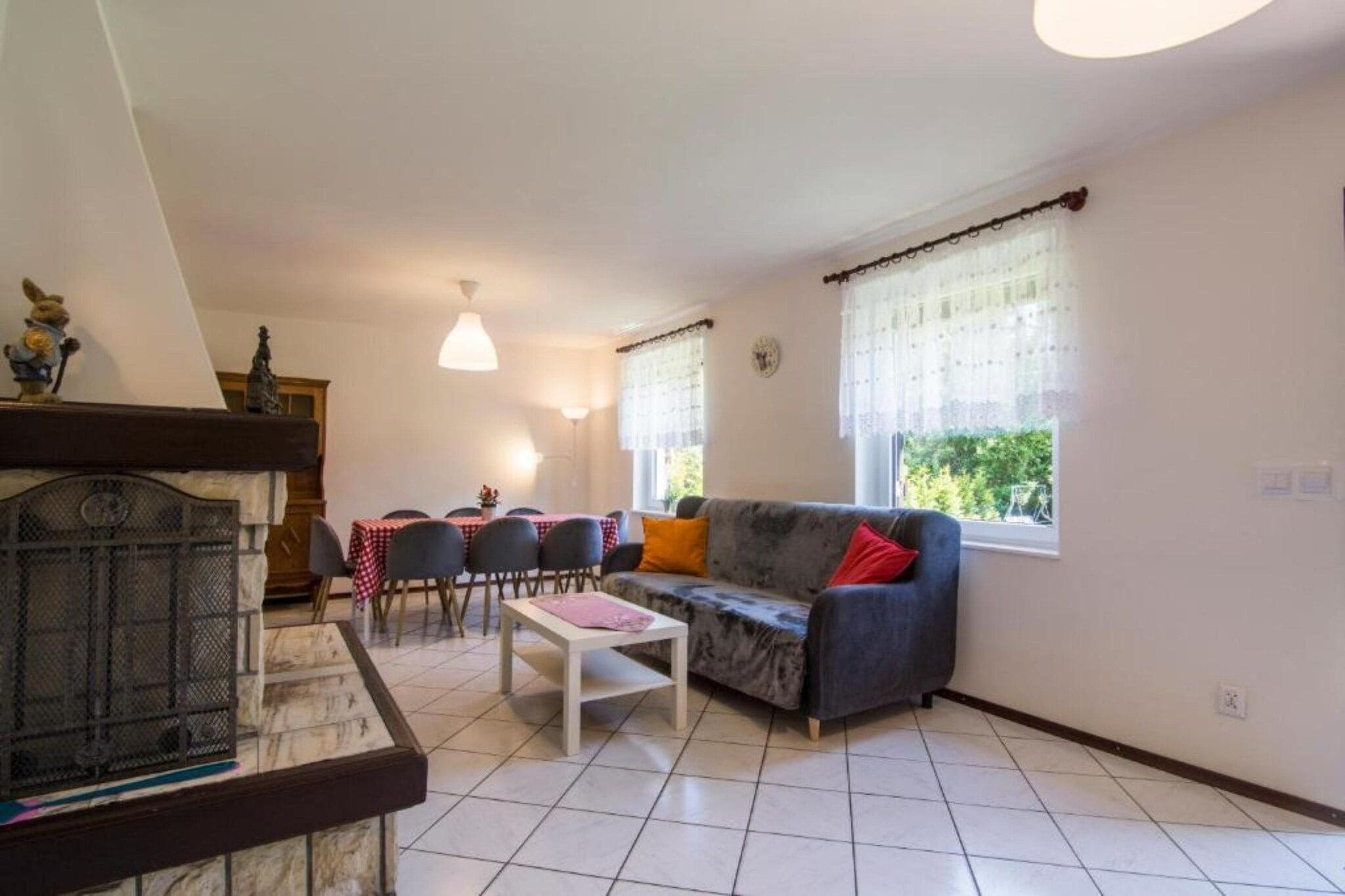 Un salon comprenant un canapé, une table basse, une table à manger avec des chaises, une cheminée et une fenêtre avec des rideaux.