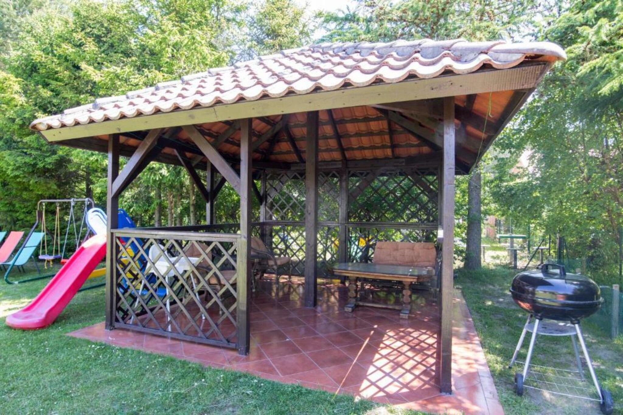 A covered outdoor area with a picnic table, a barbecue grill, and a children's slide.