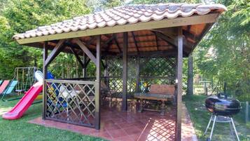 A covered outdoor area with a picnic table, a barbecue grill, and a children's slide.