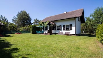 Une maison de plain-pied avec un toit en tuiles, un porche à l’avant doté d’un banc et une pelouse bien entretenue.