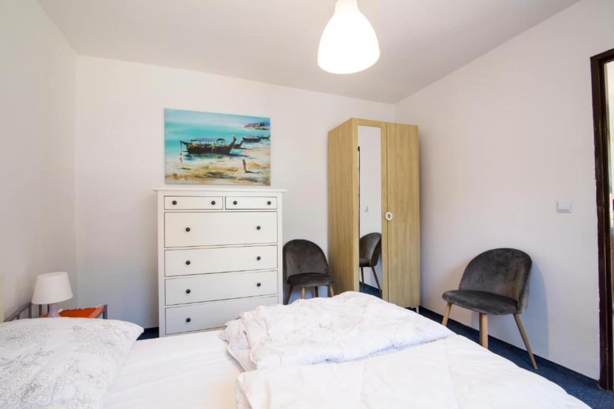 A bedroom with a bed, a dresser, two chairs, a painting, and a wardrobe.