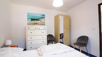 A bedroom with a bed, a dresser, two chairs, a painting, and a wardrobe.