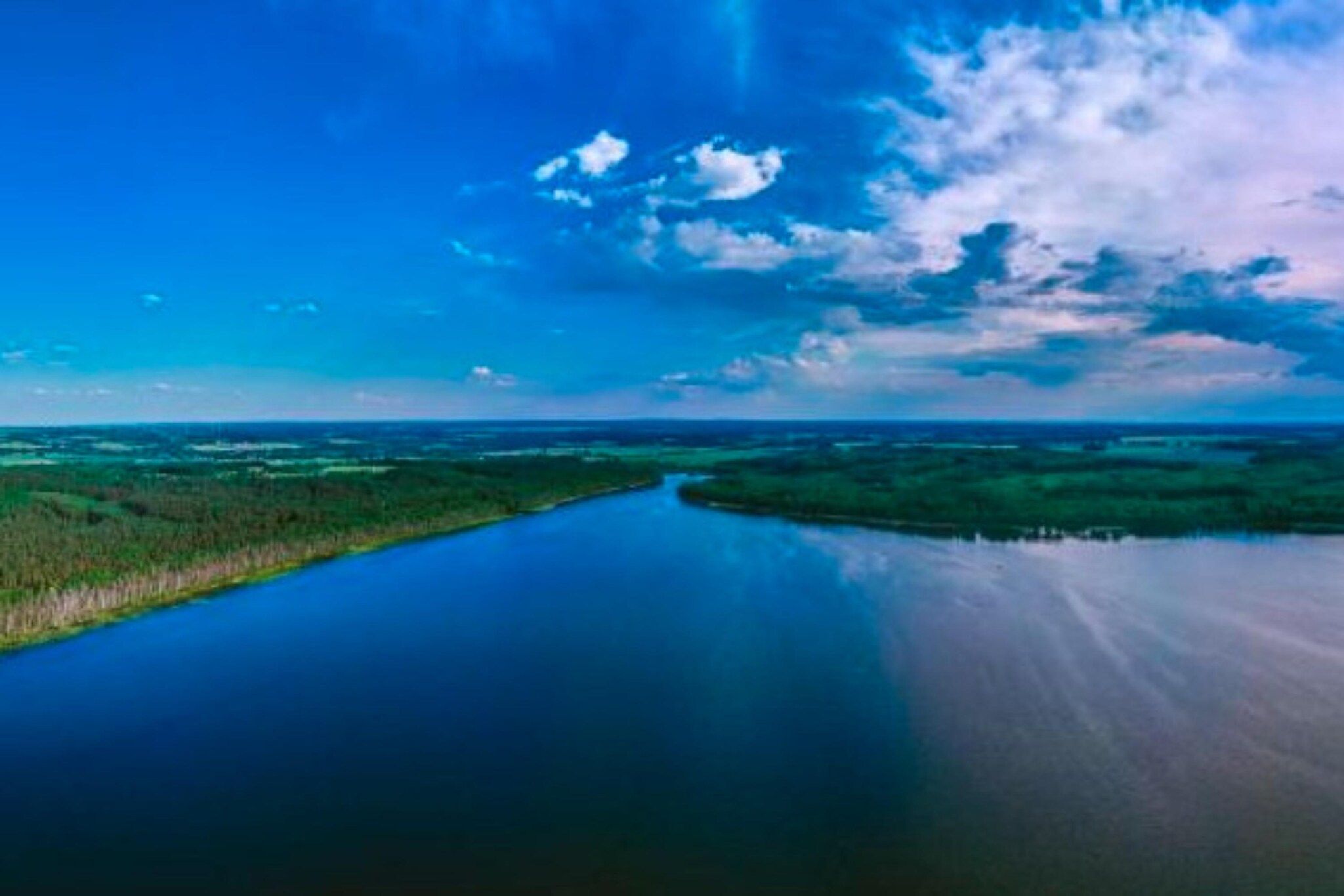 Ein Fluss mit einer schmalen Landzunge, umgeben von viel Grün und einem klaren Himmel.
