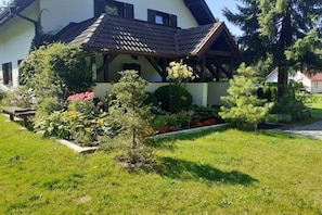 Ein Haus mit einem geneigten Dach, einer Veranda und einem gepflegten Garten mit verschiedenen Pflanzen und Blumen.