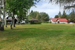 A grassy field with a gazebo, a house with a red roof, and a white building with a red roof. - Comfortable holiday home with a private garden (Lubiatowo)