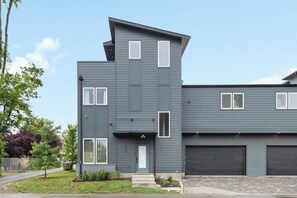 Ein modernes Wohnhaus mit zwei Etagen, flachem Dach, Hauseingang mit Tür und zwei Garagentoren.