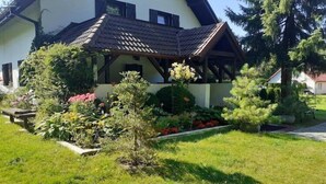 Una casa con tetto spiovente, un portico coperto e un giardino curato con diverse piante e fiori.