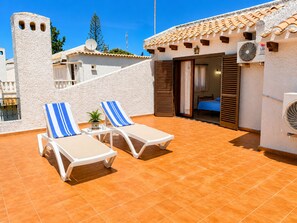 A rooftop terrace with two sun loungers, a small table with a plant, and a bedroom with a bed and curtains. - House With Garden & Beach (Orihuela)