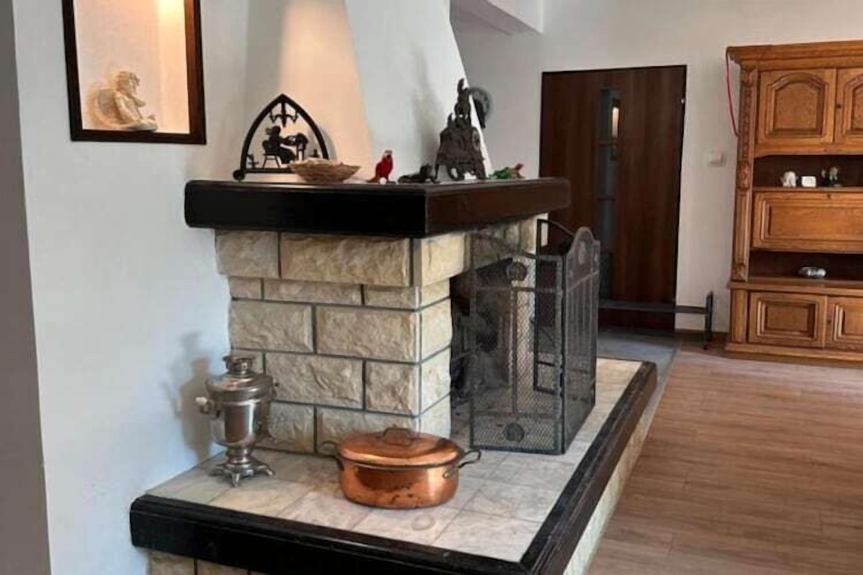 Une cheminée en pierre avec un foyer en métal, une marmite en cuivre et un samovar posés sur le manteau de la cheminée.