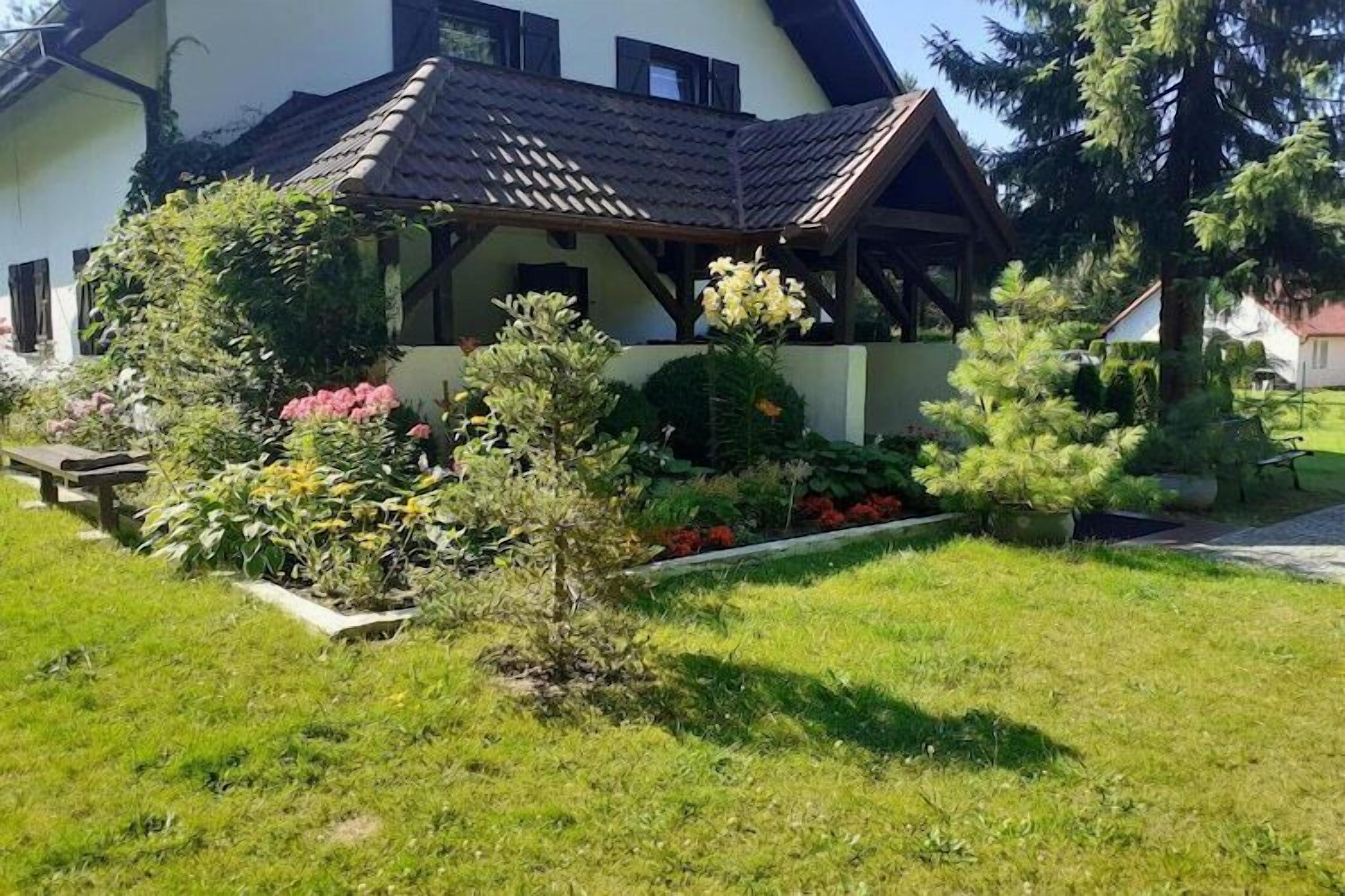 Une maison avec un toit en pente, une véranda et un jardin bien entretenu, agrémenté de diverses plantes et fleurs.