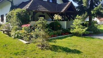 Une maison avec un toit en pente, une véranda et un jardin bien entretenu, agrémenté de diverses plantes et fleurs.