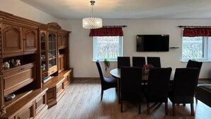A dining area with a wooden cabinet, a chandelier, and a TV mounted on the wall. - Large and comfortable holiday villa with a garden (Lubiatowo)
