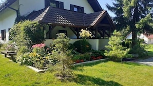 Una casa con techo inclinado, porche cubierto y un jardín cuidado con diversas plantas y flores.