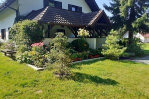Ein Haus mit einem geneigten Dach, einer Veranda und einem gepflegten Garten mit verschiedenen Pflanzen und Blumen.