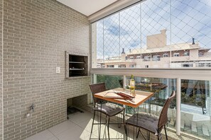 Un balcon avec un mur en briques, une table avec des chaises, une bouteille et des verres.