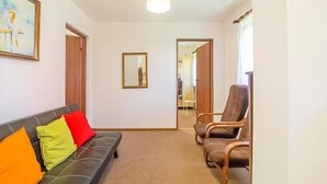 Una habitación con sofá, dos sillones, un espejo y una puerta que da a otra estancia.
