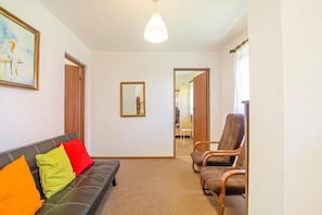 Une pièce comprenant un canapé, deux fauteuils, un miroir et une porte donnant sur une autre pièce.