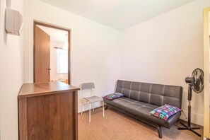 A room with a wooden desk, a grey chair, a black sofa with colorful cushions, and a standing fan. - Single-story holiday home with a private garden (Lubiatowo)
