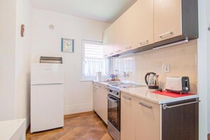 A compact kitchen with a refrigerator, oven, and a window with blinds.